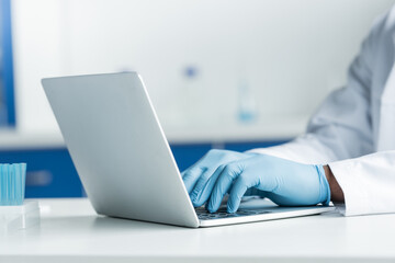 Cropped view of african american scientist in latex gloves using laptop near test tubes