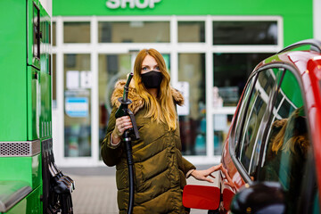Woman wear medical mask at self-service gas station, hold fuel nozzle, refuel the car with petrol...