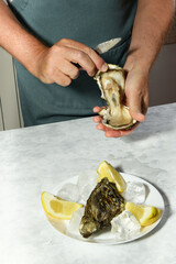 A man's hands are shucking fresh oysters with a blade of knife, Opening the hollow and flat oysters. Chef opens raw oysters in the restaurant, lifestyle. ready to eat on light background, luxury food