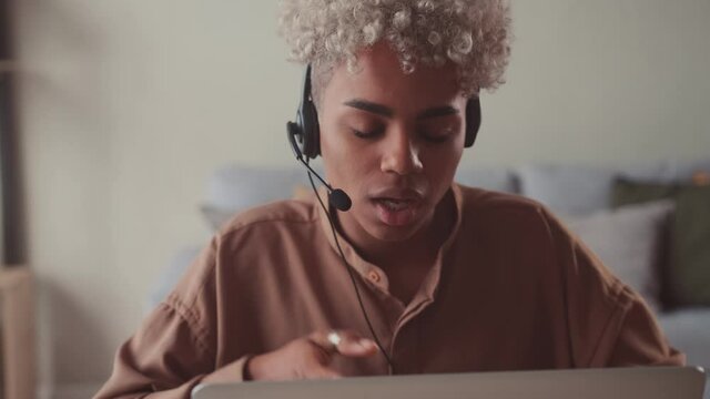 Close up pleasant young African American curly haired woman in headset takes call customer service responding to customer inquiry, call center worker or support operator smiling friendly.