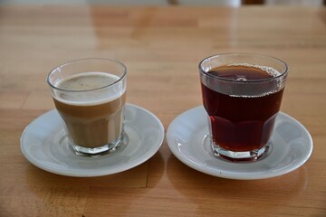 Two transparent glasses with coffee and tea on white saucers