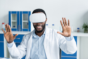 Naklejka premium Smiling african american doctor in virtual reality headset in clinic