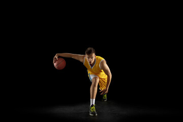 Fototapeta na wymiar Basketball player with a ball training isolated on dark black studio background. Advertising concept. Fit Caucasian athlete practicing with ball.