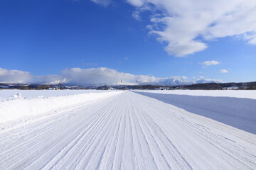 真っ直ぐに伸びた真っ白な道とその先に見える十勝岳連峰