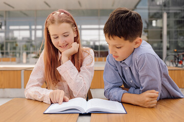 Primary secondary education, school, concept of friendship - two students boy and teenage girl with backpacks are sitting, talking after school with book and bug