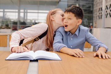 Naklejka premium teenage schoolgirl girl is whispering something in boy's ear or kissing him.
