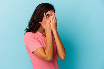 Young caucasian woman isolated on blue background blink through fingers frightened and nervous.