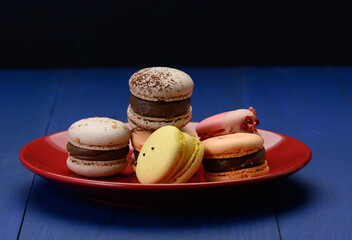 baked almond macarons on a red ceramic plate, blue background