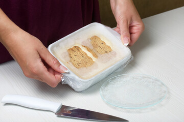 A woman holds homemade ice cream in her hands. Cookies and cream. Packaged in plastic wrap. Close-up shot.