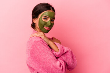 Young caucasian woman wearing a bathrobe and facial mask isolated on pink background