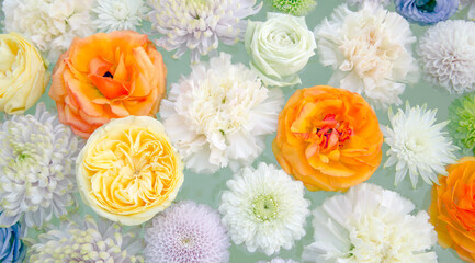 Flower arrangement of chrysanthemums, carnations, roses and ranunculus. White, yellow, orange, and purple flowers floating on water.