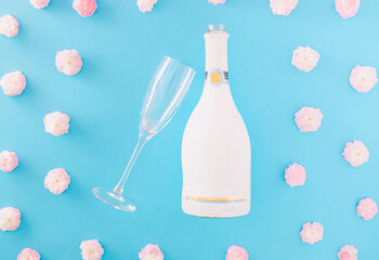 Champagne bottle and champagne glass surrounded by the light pink flowers on a pastel blue background. Delicate creative celebrating idea.