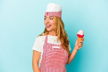 Caucasian ice cream maker woman holding an ice cream isolated on blue background looks aside smiling, cheerful and pleasant.