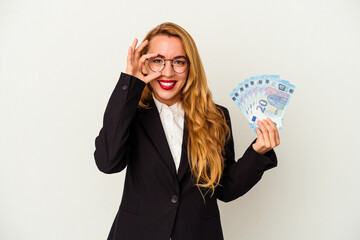 Caucasian business woman holding bills isolated on white background excited keeping ok gesture on eye.