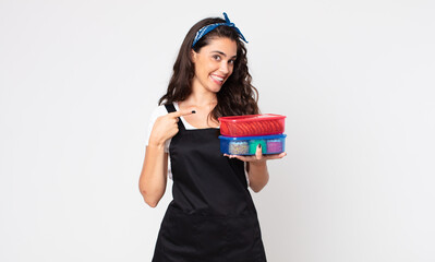 pretty woman smiling cheerfully, feeling happy and pointing to the side and holding tupperwares with food - obrazy, fototapety, plakaty