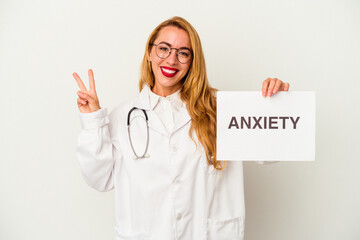 Caucasian doctor woman holding a anxiety placard isolated on white background joyful and carefree showing a peace symbol with fingers.