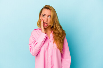 Caucasian woman isolated on blue background is saying a secret hot braking news and looking aside