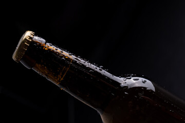Dark glass beer bottle with condensation drops on black background.