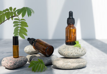 Bottles of dark amber glass of lotion or essential oil on gray stones. Natural SPA cosmetic products background. Layout of the beauty salon branding