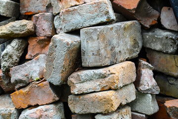 A pile of old red and orange bricks in the grass near the log cabin wall and covered with black film.