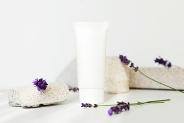 plastic cosmetic tube with face cream or body lotion on a white stone stand with lavender flowers. Spa cosmetics concept with natural herbs