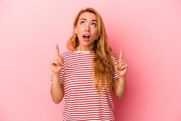 Caucasian blonde woman isolated on pink background pointing upside with opened mouth.