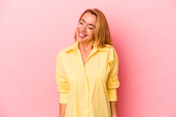 Caucasian blonde woman isolated on pink background laughs and closes eyes, feels relaxed and happy.