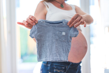 Happy pregnant mother is holding little blue baby shirt