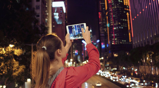 Young woman taking photos of buildings on her tablet pc at night, Hong Kong.