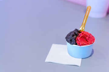 Small blue cup of dark chocholate  and raspberry ice cream in shop on a blue table