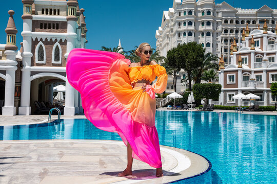 Summer fashion. Sexy fashion model. Glamour, stylish sexy blonde female model in summer elegant colorful dress near the pool. Travel model in a luxury hotel in the Turkish resort.