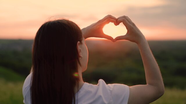 Girl made love heart out of her palms. Young Woman enjoying summer, relaxing. Carefree chewing girl making heart shape with her fingers. Light of summer spring sun on hands. Travel and relax in nature
