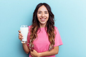 Young mixed race woman holding a glass of milk isolated on blue background laughing and having fun.
