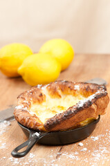 top, front view, close distance, of a German pancake, taken off heat, in a black, cast iron fry pan, with three lemons on a wood cutting board