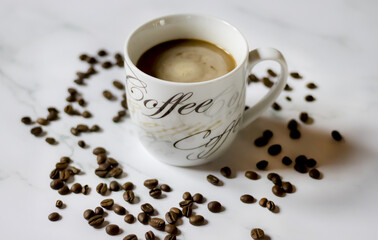 Photo of a coffee cup with coffee beans scattered around it on a white table