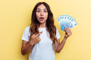 Young mixed race woman holding bills isolated on yellow background pointing to the side