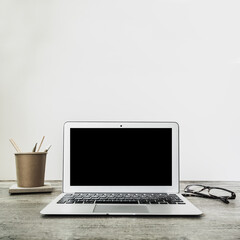 Fototapeta premium Laptop with blank black screen on wooden desk. Home interior or office background. Copy space.