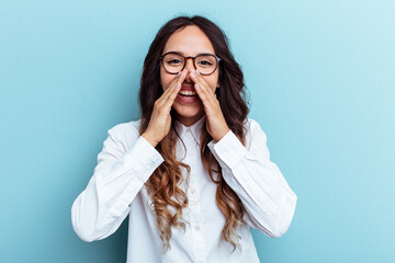 Young mexican woman isolated on blue background saying a gossip, pointing to side reporting something.