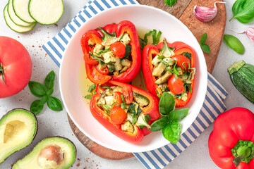 Baked peppers stuffed with vegetables in a plate on a gray concrete background. Baked peppers with zucchini, avocado, tomatoes and basil. Vegan or diet food.