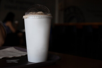 White paper cup with creamy coffee in dark cafe interior. Blank paper mug coffee shop branding mockup. Cafe business identity. White paper mug for coffee logo. Dark cafe interior