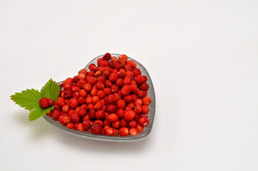 wild strawberries in a heart-shaped bowl on a white background and place for text