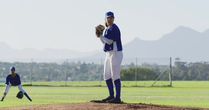 Caucasian female baseball player wearing glasses pitching ball on baseball field