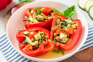 Baked peppers stuffed with vegetables in a plate on a gray concrete background. Baked peppers with zucchini, avocado, tomatoes and basil. Vegan or diet food.