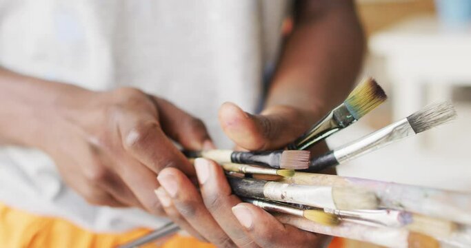 Midsection of african american male painter holding brushes in artist studio