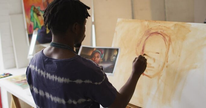African american male painter painting from photograph on canvas in artist studio