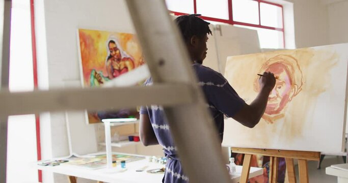 Rear view of african american male artist wearing apron painting on canvas at art studio