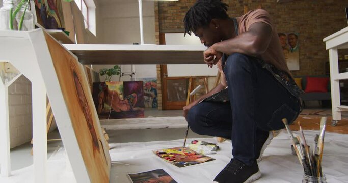Side view of african american male artist wearing apron painting on canvas at art studio