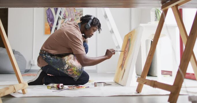 African american male artist wearing headphones painting on canvas at art studio