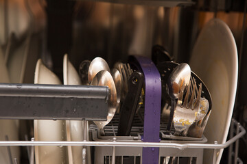 Close-up on dirty plates and cutlery. The plates and cutlery are in the dishwasher and are ready to...