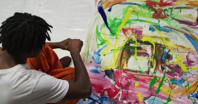 Overhead view of african american male artist pouring paint with a paint brush on canvas